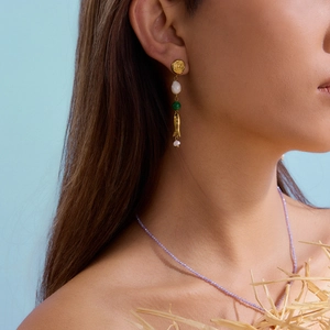 Detailed view of long gold drop earring with pearl, green bead, and fish charm on a model