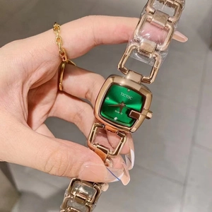 Close-up of golden square watch with emerald green dial and elegant link bracelet