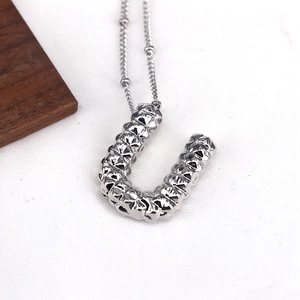 Detail of silver U-shaped letter pendant with textured diamond faceted surface on white fabric
