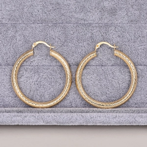 Dettaglio ravvicinato di orecchini a cerchio dorati con una raffinata trama metallica a tratteggio