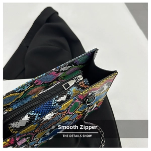Close-up of smooth metal zipper and silver chain on colorful snakeskin shoulder bag