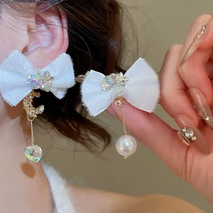 Detail of white fabric bow earrings with pearl pendants and crystal star moon accents