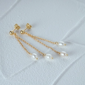 Macro shot of gold tassel earrings with drop pearls on a textured white stone surface