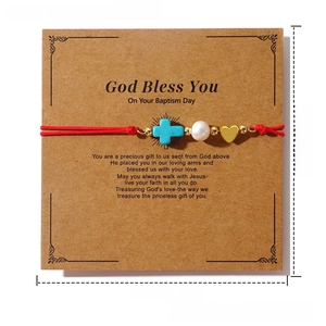 Detail of red rope bracelet with blue cross, white pearl and gold heart on card