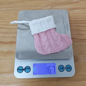 Pink and white knit Christmas stocking being weighed on a scale showing 16.7g mass
