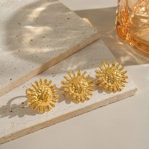 Macro shot of three golden hammered texture sun-shaped stud earrings on stone