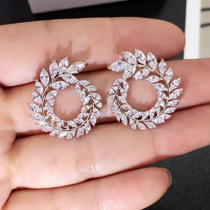 Close-up of hand holding silver olive leaf hoop earrings with sparkly zircon stones