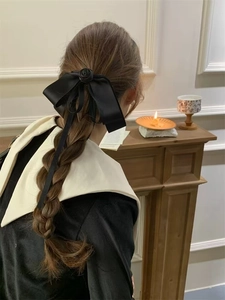 Elegant black satin bow hair clip with rose detail worn on a braided hairstyle