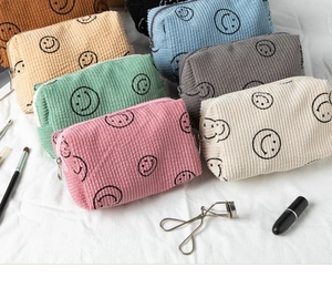 Detailed pile of colorful corduroy makeup bags with smiley face prints and top zippers