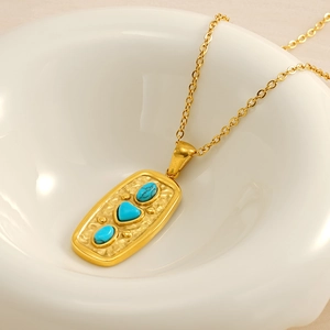 Detailed shot of gold stainless steel necklace with heart turquoise pendant on ceramic