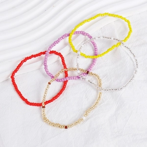 Detail view of multi-colored Bohemian seed bead bracelets stacked on a white textured surface