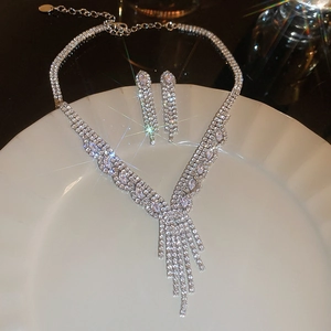 Detailed view of silver necklace and drop earrings set with crystals on ceramic plate