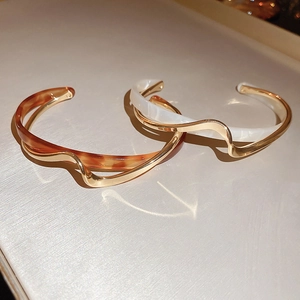Detailed view of wave-shaped gold-plated open bracelets with amber and marble resin inlay
