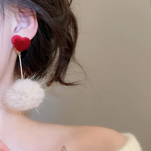 Détail d'une boucle d'oreille cœur avec pendentif pompon blanc sur le profil d'un modèle