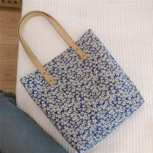 Detail of floral canvas tote bag featuring reinforced leather handles and golden rivets