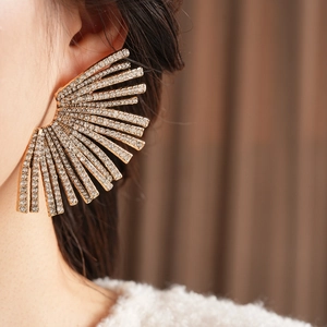 Macro detail of a large golden fan-shaped earring with crystals on a female model