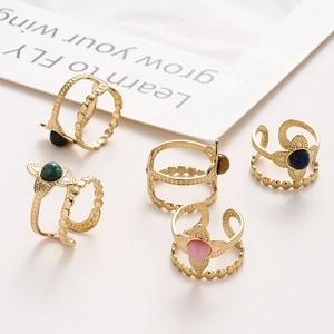 Set of five gold flower rings with green pink blue and black gemstones on white surface