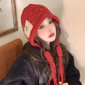 Detail of red knitted mohair beanie with ear flaps and long tassels worn by a model