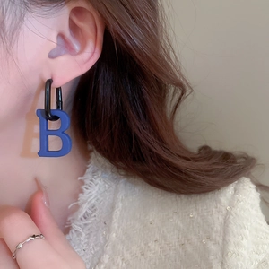 Close-up of blue letter B pendant earrings with black ear clips on model wearing a jacket