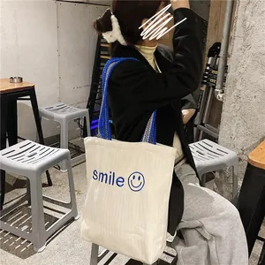 Detail of canvas tote bag featuring blue smile embroidery and ethnic patterned strap