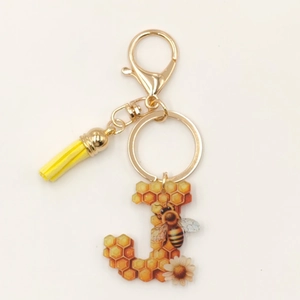Detail of letter J honey bee keychain with acrylic honeycomb design and yellow tassel