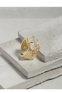 Makro-Detail des goldenen Rings mit großem unregelmäßigem Kristall auf grauen Steinplatten