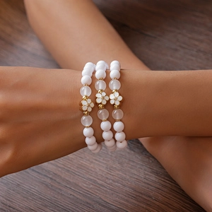 Close-up of three acrylic beaded bracelets with gold-edged white flower pendants