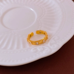 Détail d'une bague ouverte dorée avec zircons en cœur sur une assiette blanche