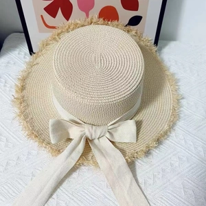 Close-up of beige raffia boater hat with frayed edges and long white ribbon bow