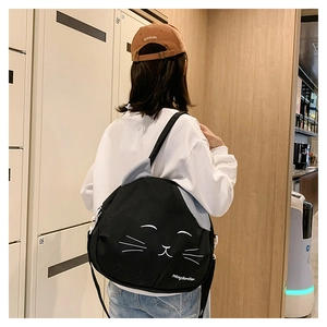 Rear view of a black cat-shaped canvas shoulder bag worn by a model in casual wear