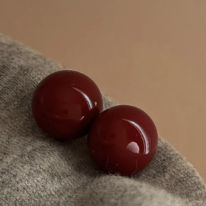 Macro view of deep red round pearl stud earrings placed on a soft grey knitted fabric