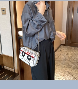 Close-up of white cassette-shaped crossbody bag with gold chain strap and vintage tape print