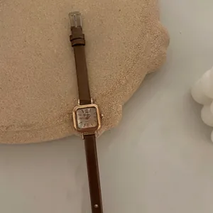 Close-up of square rose gold quartz watch with brown leather strap and cream dial