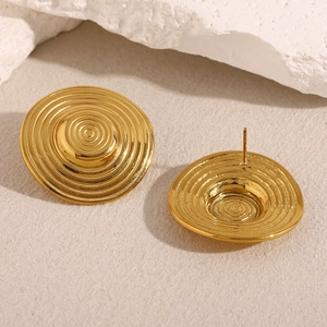 Detail of 18K gold-plated concentric spiral earrings on a natural white stone base