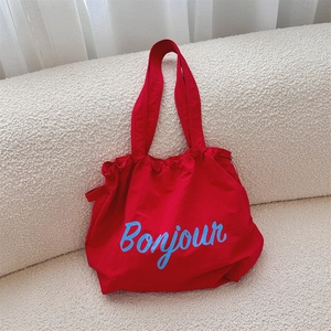 Detailed view of a red canvas tote bag with Bonjour print on a white fleece texture sofa