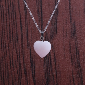 Polished pink quartz heart pendant necklace with a slim silver chain on dark background