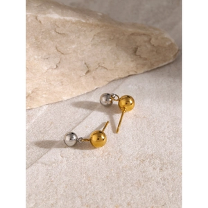 Détail macro de boucles d'oreilles boules bicolores or 18k et argent sur fond pierre