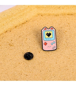 Detail of pink game console enamel pin with black heart on cork background