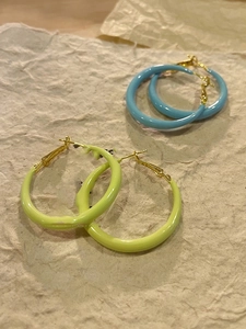 Detail view of light blue and green enamel hoop earrings on textured paper background
