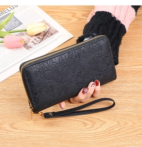 Detail of black long zipper wallet with floral embossing held by a hand on a desk