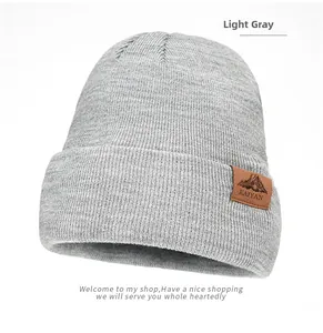 Detail of light gray knit beanie with a brown leather mountain logo patch on the cuff