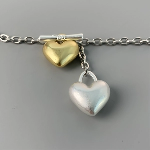Detail of OT buckle necklace with gold and silver heart pendants on a metal chain