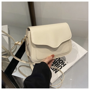 Detail of minimalist beige crossbody bag featuring sleek curved flap and gold hardware