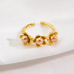 Golden flower titanium steel ring with champagne pearls on white fabric background