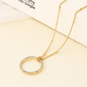 Dettaglio del ciondolo circolare dorato con micro-pavé di cristalli e catena a sfere d'oro