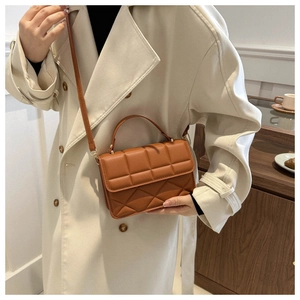 Brown quilted crossbody bag with top handle and shoulder strap styled on a trench coat