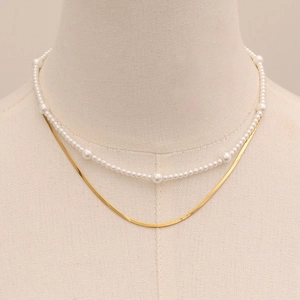Close-up of double-layered necklace with white pearls and golden snake chain on a model
