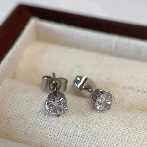 Macro detail of classic round-cut zircon studs with silver prong settings on beige fabric