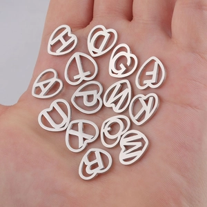 Stainless steel silver heart-shaped hollow alphabet charms held in hand for DIY jewelry