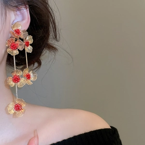 Close-up of golden hollow flower tassel earrings with red rose detail and layered petals